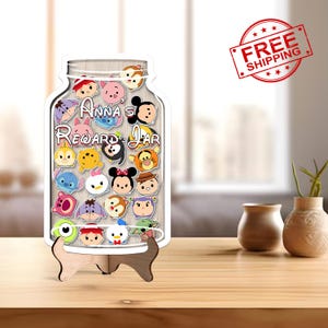 May include: A wooden reward jar in the shape of a mason jar, filled with colorful Disney Tsum Tsum characters. The jar has the text "Anna's Reward Jar" and sits on a wooden stand. The background is a blurred interior scene.