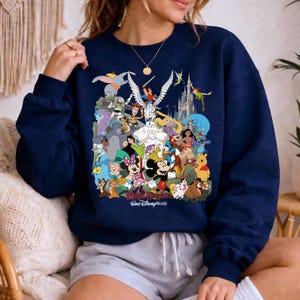 Puede incluir: Sudadera azul marino con un collage colorido de personajes de Disney, incluyendo Mickey Mouse, Minnie Mouse y Dumbo. Las palabras "Magic Kingdom" y "Walt Disney World" est&aacute;n impresas en la parte inferior del dise&ntilde;o.