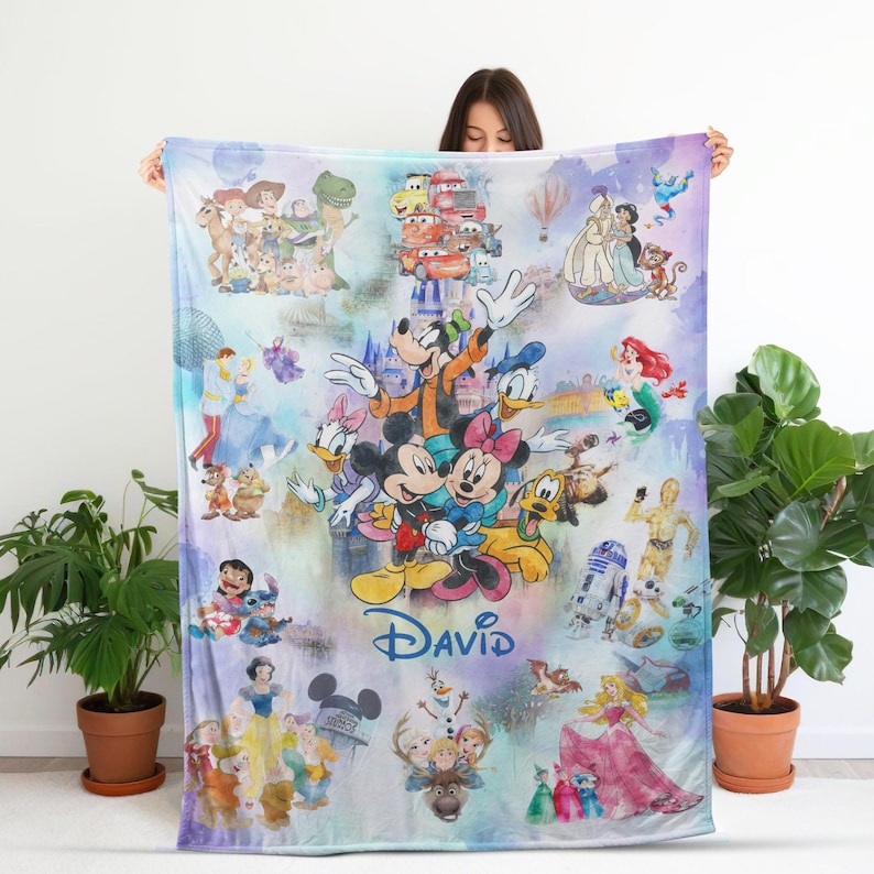 Op de afbeelding: Een kleurrijke deken met verschillende Disney-personages, waaronder Mickey en Minnie Mouse, Goofy, Donald Duck en personages uit Star Wars en Disney Princess-films. De naam "DAVID" is in blauwe letters geschreven.