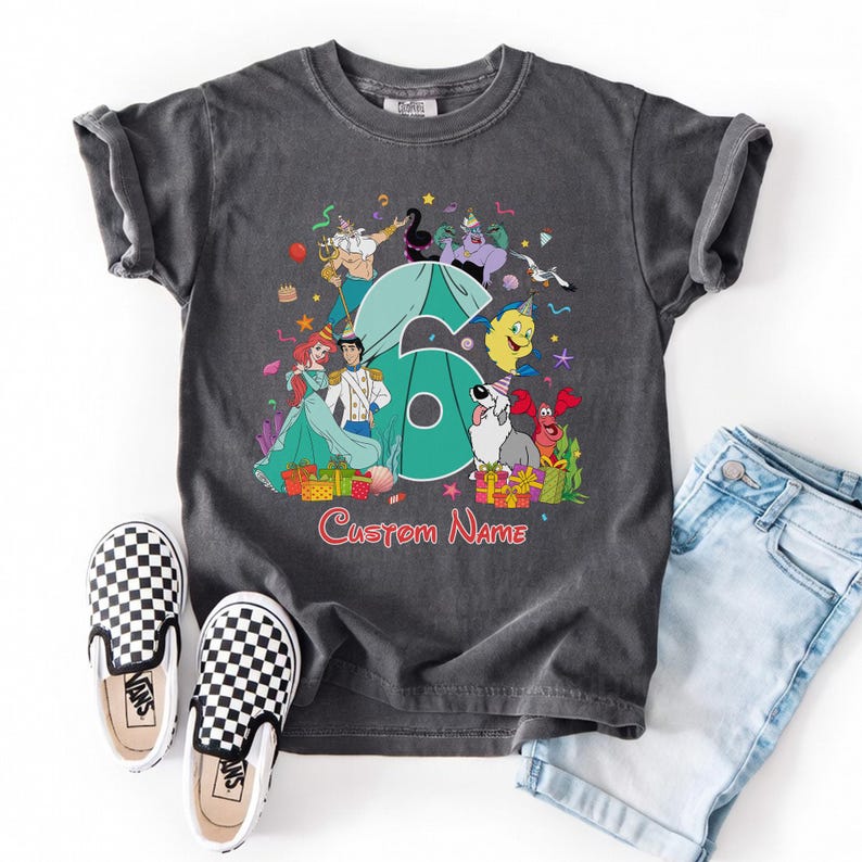 K&ouml;nnte beinhalten: Ein anthrazitfarbenes Kurzarm-T-Shirt mit einer gro&szlig;en t&uuml;rkisfarbenen Zahl sechs, umgeben von bunten Zeichentrickfiguren aus Arielle, die Meerjungfrau, darunter Arielle, Eric, Fabius und Sebastian, mit dem roten Text Custom Name darunter.