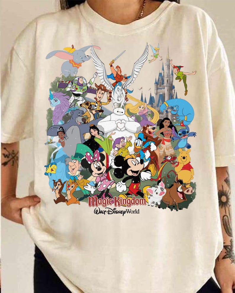 Puede incluir: Camiseta color crema con un gr&aacute;fico colorido de varios personajes de Disney, incluyendo Mickey y Minnie Mouse, Dumbo y Peter Pan. Las palabras "Magic Kingdom" y "Walt Disney World" est&aacute;n impresas debajo.