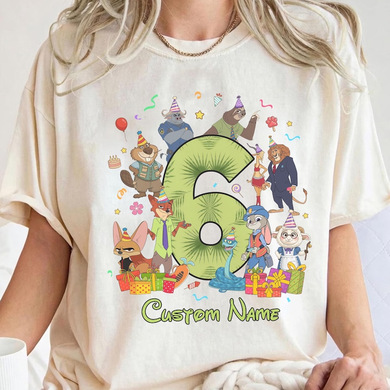 May include: A cream-colored t-shirt featuring a large green number six surrounded by various cartoon animal characters wearing party hats. The design includes colorful gift boxes, balloons, and the text Custom Name printed in green at the bottom.