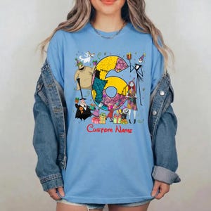 May include: A light blue t-shirt featuring a large yellow number six decorated with patterns, surrounded by characters from The Nightmare Before Christmas including Jack Skellington, Sally, and Oogie Boogie, with the red text Custom Name below.