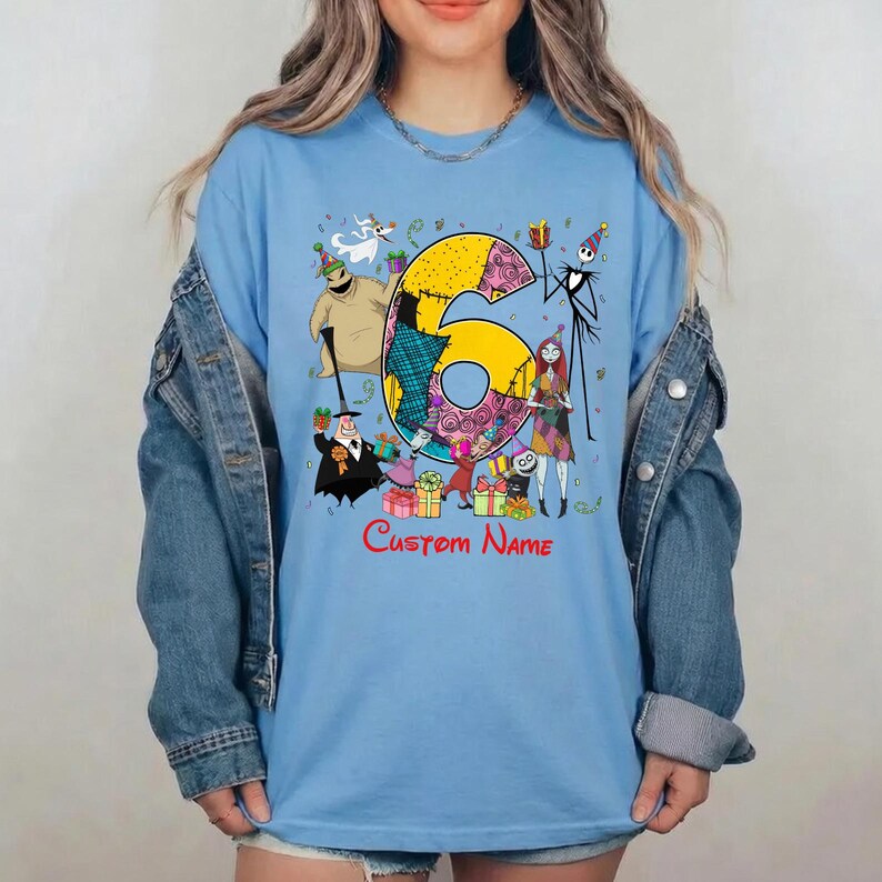 May include: A light blue t-shirt featuring a large yellow number six decorated with patterns, surrounded by characters from The Nightmare Before Christmas including Jack Skellington, Sally, and Oogie Boogie, with the red text Custom Name below.