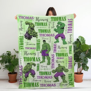 May include: A light green blanket featuring multiple illustrations of the Hulk in various poses, interspersed with the name "Thomas" in green and white. The blanket has a watercolor-like background.