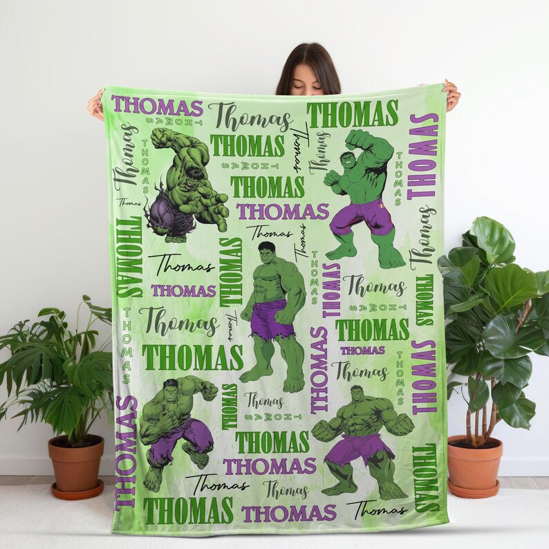 May include: A light green blanket featuring multiple illustrations of the Hulk in various poses, interspersed with the name "Thomas" in green and white. The blanket has a watercolor-like background.