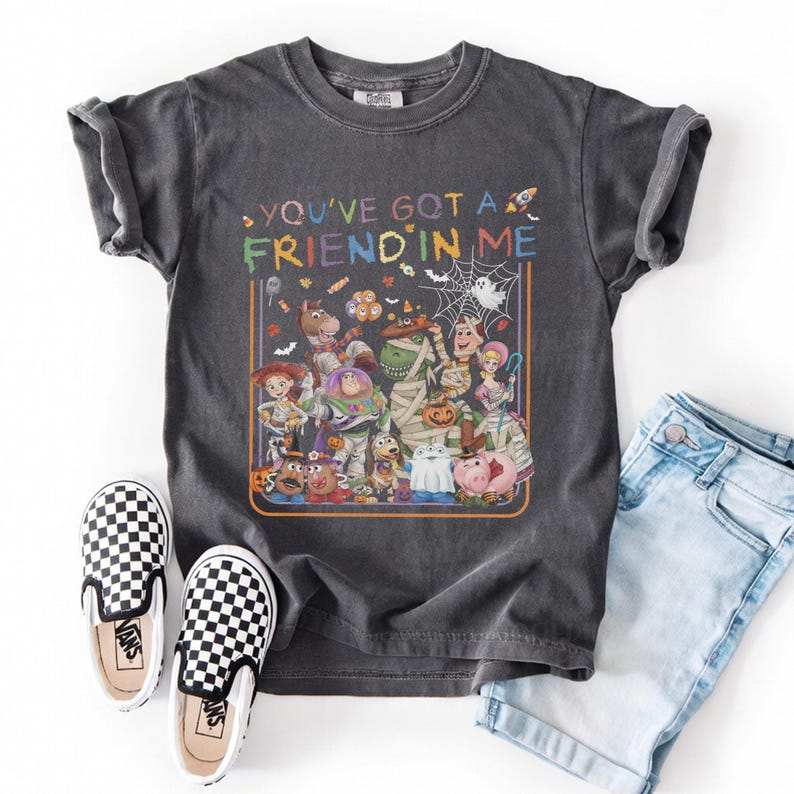 K&ouml;nnte beinhalten: Ein anthrazitfarbenes Kurzarm-T-Shirt mit einer bunten Grafik verschiedener Zeichentrickfiguren in Halloween-Kost&uuml;men. Der Text "YOU'VE GOT A FRIEND IN ME" ist &uuml;ber den Figuren aufgedruckt, erg&auml;nzt durch Motive von S&uuml;&szlig;igkeiten und Spinnenweben.