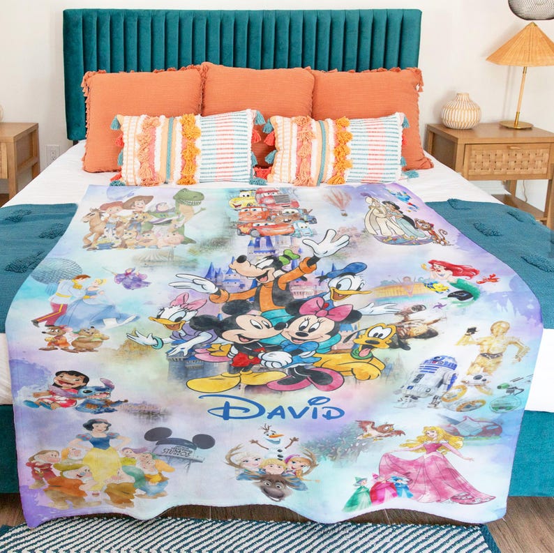 Op de afbeelding: Een kleurrijke deken met Disney-personages, waaronder Mickey Mouse, Minnie Mouse, Donald Duck en Goofy. De deken heeft de gepersonaliseerde naam "DAVID" en bevat afbeeldingen van prinsessen en andere personages.