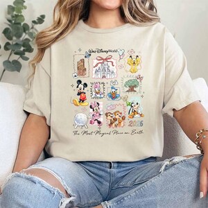 Puede incluir: Camiseta beige con un gr&aacute;fico colorido de personajes y lugares emblem&aacute;ticos de Disney World. El dise&ntilde;o incluye a Mickey Mouse, Minnie Mouse, Donald Duck y Chip y Chop, con el texto "Walt Disney World" y "2026". Tambi&eacute;n se incluye la frase "The Most Magical Place on Earth".