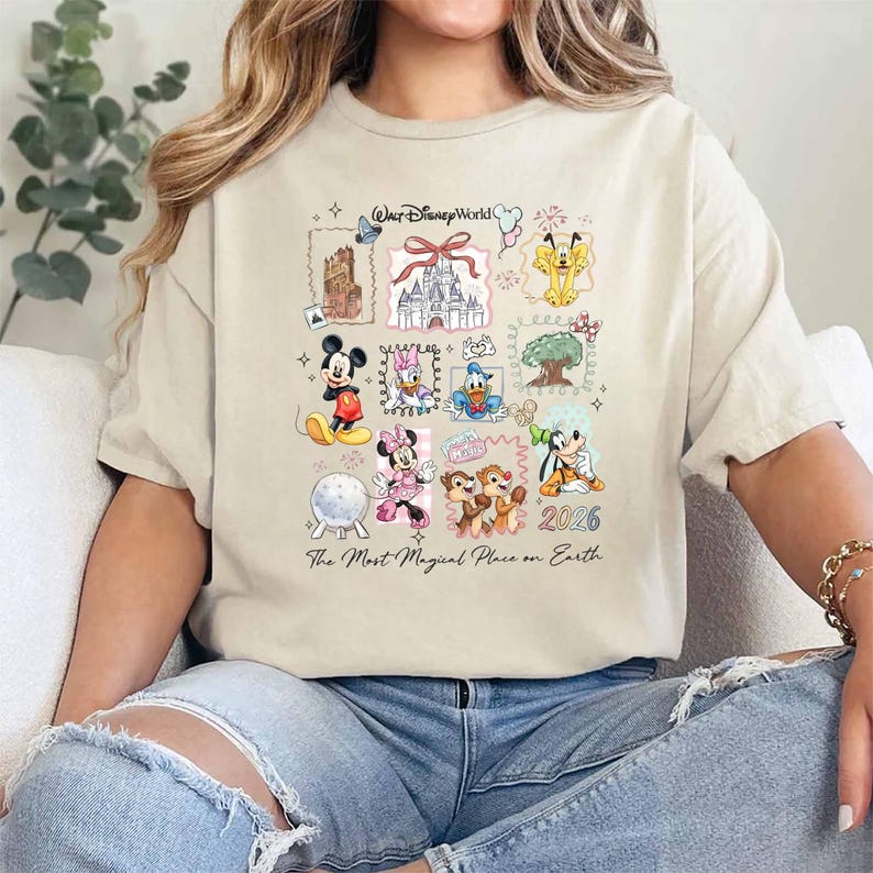 Puede incluir: Camiseta beige con un gr&aacute;fico colorido de personajes y lugares emblem&aacute;ticos de Disney World. El dise&ntilde;o incluye a Mickey Mouse, Minnie Mouse, Donald Duck y Chip y Chop, con el texto "Walt Disney World" y "2026". Tambi&eacute;n se incluye la frase "The Most Magical Place on Earth".