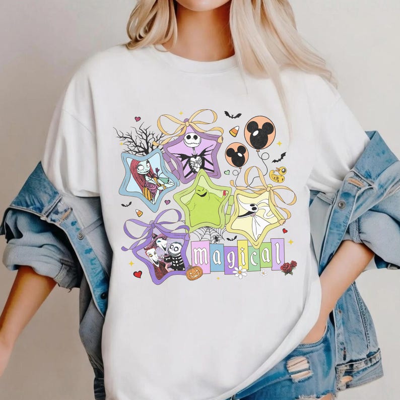 May include: White t-shirt with a colourful graphic featuring characters from The Nightmare Before Christmas. The design includes star-shaped frames, bows, and the word "magical".