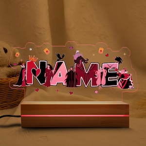 May include: A personalized night light with the name "NAME" illuminated in pink. The design features cartoon villains and decorative hearts, stars, and crowns. The light sits on a wooden base with a red glow.