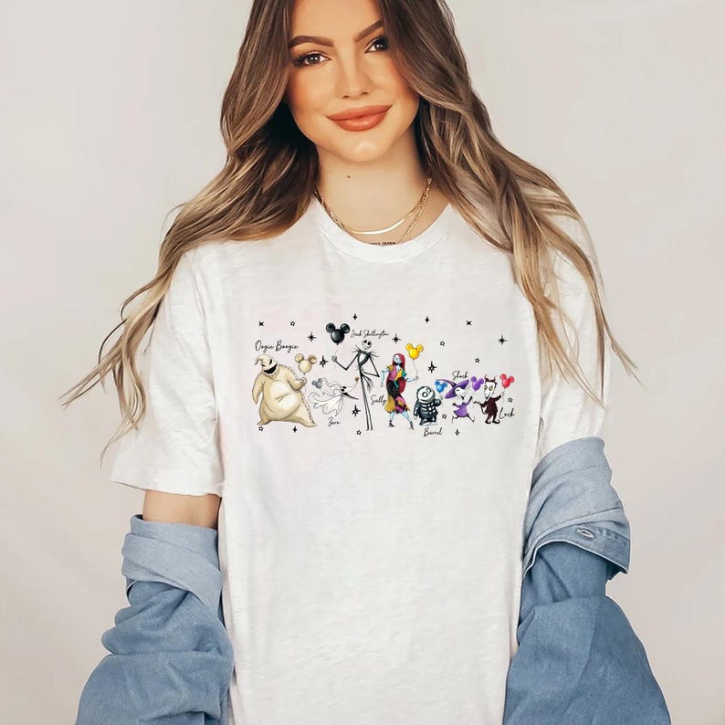 K&ouml;nnte beinhalten: Wei&szlig;es T-Shirt mit einer farbenfrohen Grafik von Charakteren aus The Nightmare Before Christmas, darunter Jack Skellington, Sally und Oogie Boogie. Das Design enth&auml;lt Charakternamen und Sternakzente.