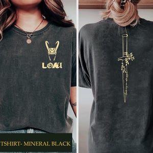 May include: Dark gray t-shirt with a gold Loki design on the front and a gold dagger illustration on the back. The front features the Loki helmet and the word "LOKI". The back has the text "Love is a dagger".