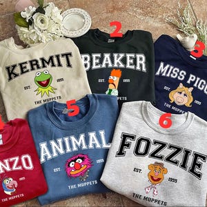 Puede incluir: Seis sudaderas de cuello redondo con personajes de los Muppets: Kermit, Beaker, Miss Piggy, Gonzo, Animal y Fozzie. Cada sudadera tiene el nombre del personaje en negrita, el año 1955 y el texto "The Muppets". Las sudaderas son de varios colores.