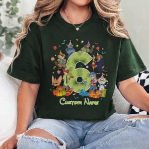 May include: A dark green short-sleeve t-shirt featuring a large light green number six surrounded by various cartoon animal characters wearing party hats. The graphic includes colorful gift boxes, confetti, and the text Custom Name at the bottom.