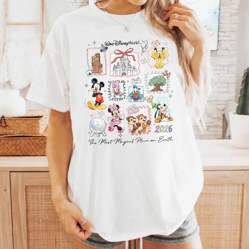 Puede incluir: Camiseta blanca con un colorido gr&aacute;fico de Disney World. El dise&ntilde;o incluye varios personajes y lugares emblem&aacute;ticos de Disney, con el texto "Walt Disney World", "The Most Magical Place on Earth" y el a&ntilde;o "2026".