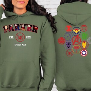 Puede incluir: Sudadera con capucha verde oliva con la palabra "PARKER" y la imagen de Spider-Man. La parte trasera muestra varios logotipos de superh&eacute;roes en un patr&oacute;n hexagonal. Tambi&eacute;n se ve el texto "EST. 2001 SPIDER MAN".