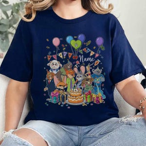 Puede incluir: Camiseta azul marino con un dise&ntilde;o de cumplea&ntilde;os colorido. El dise&ntilde;o incluye personajes de dibujos animados, globos, una tarta, el n&uacute;mero 6 y la palabra "Name". Una camiseta gr&aacute;fica festiva y personalizada.