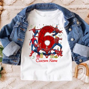 May include: A white short-sleeved t-shirt featuring a large red number six with a spiderweb pattern, surrounded by multiple Spider-Man figures wearing party hats, colourful gift boxes, and confetti, with the red text Custom Name below.