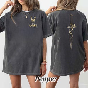 May include: Dark gray t-shirt with gold-colored graphics. The front features a stylized design and the word "LOKI". The back displays a dagger design with floral accents and the text "wedding in trust". The word "Pepper" is at the bottom.