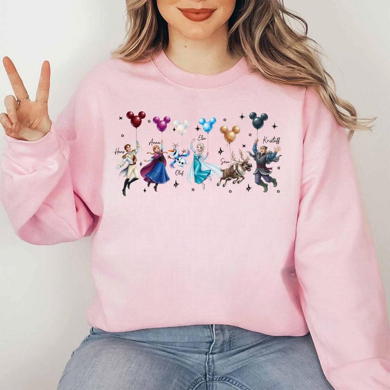 May include: Pink sweatshirt featuring Disney's Frozen characters holding Mickey Mouse balloons. The characters include Hans, Anna, Elsa, Olaf, Sven, and Kristoff. The names of the characters are printed above them.