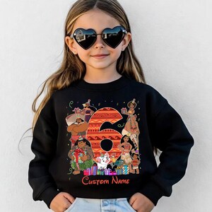 May include: A black long-sleeve sweatshirt featuring a large orange number six with a tribal pattern. The graphic includes various animated characters, colorful gift boxes, and party hats. Below the graphic, the text Custom Name is printed in red.