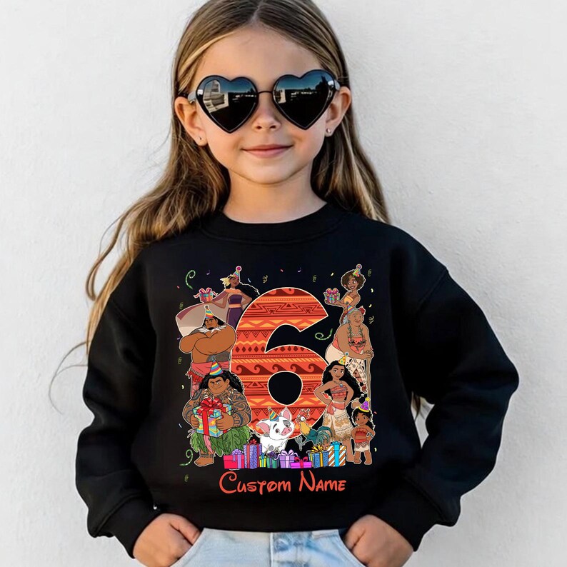 May include: A black long-sleeve sweatshirt featuring a large orange number six with a tribal pattern. The graphic includes various animated characters, colorful gift boxes, and party hats. Below the graphic, the text Custom Name is printed in red.