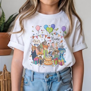 Puede incluir: Camiseta blanca con un dise&ntilde;o de cumplea&ntilde;os colorido con personajes de dibujos animados, globos, confeti y una tarta de dos pisos. El dise&ntilde;o incluye el n&uacute;mero 6 y espacio para un nombre. La camiseta la lleva una persona.