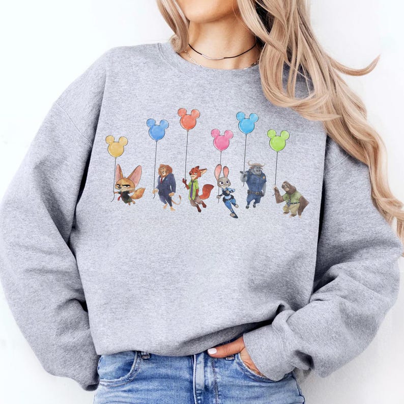 May include: A light gray sweatshirt featuring a colorful graphic of cartoon characters holding Mickey Mouse-shaped balloons. The characters are from the animated movie Zootopia. The balloons are yellow, blue, orange, pink, and green.