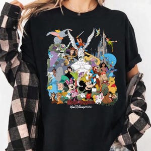 Puede incluir: Camiseta negra con un gr&aacute;fico colorido de varios personajes de Disney, incluyendo Mickey y Minnie Mouse, Dumbo y Peter Pan. Tambi&eacute;n se puede ver el texto "Magic Kingdom Walt Disney World".