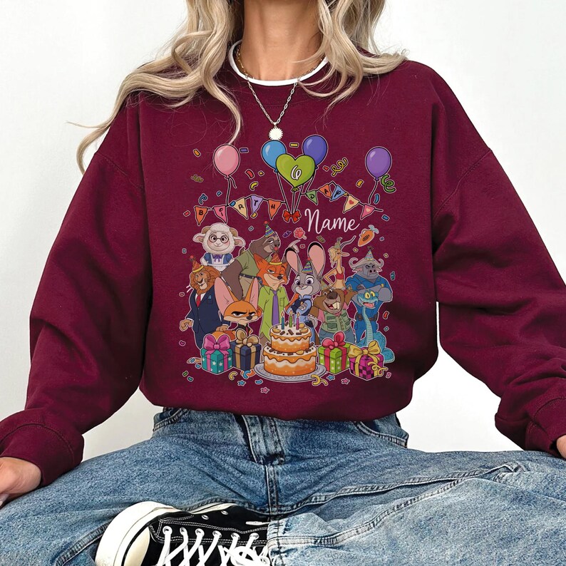 Puede incluir: Sudadera burdeos con un gr&aacute;fico colorido de personajes de dibujos animados, globos y una tarta de cumplea&ntilde;os. El dise&ntilde;o incluye la palabra "Name" y decoraciones festivas, creando un tema de celebraci&oacute;n. La sudadera es de color burdeos liso.