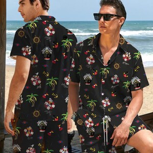 May include: Black shirt and shorts co-ord set with a nautical theme. The set features cartoon characters, anchors, life preservers, palm trees, and ship wheels. The shirt has short sleeves and a button-down front. The shorts have a drawstring waist.