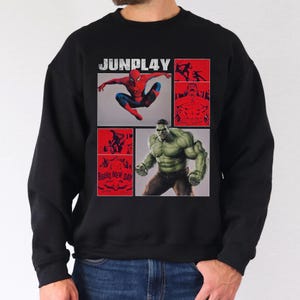 Op de afbeelding: Zwart sweatshirt met een grafisch ontwerp met Spider-Man en de Hulk, met de tekst "JUNPLAY". Het ontwerp bevat rode en witte elementen, en de woorden "BRAND NEW DAY" zijn ook zichtbaar.