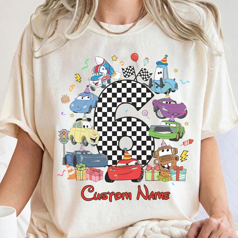 May include: A cream-coloured t-shirt with a vibrant cartoon car design, featuring the number 6 in a chequered pattern. The design includes the text "Custom Name" in red, ideal for a birthday celebration.