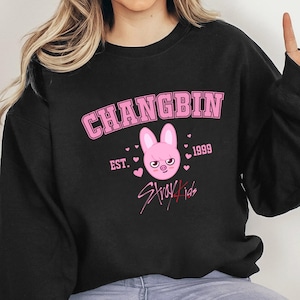 May include: Black sweatshirt featuring a pink graphic. The design includes the name "CHANGBIN", the year "1999", a bunny face, the text "Stray Kids", and hearts.