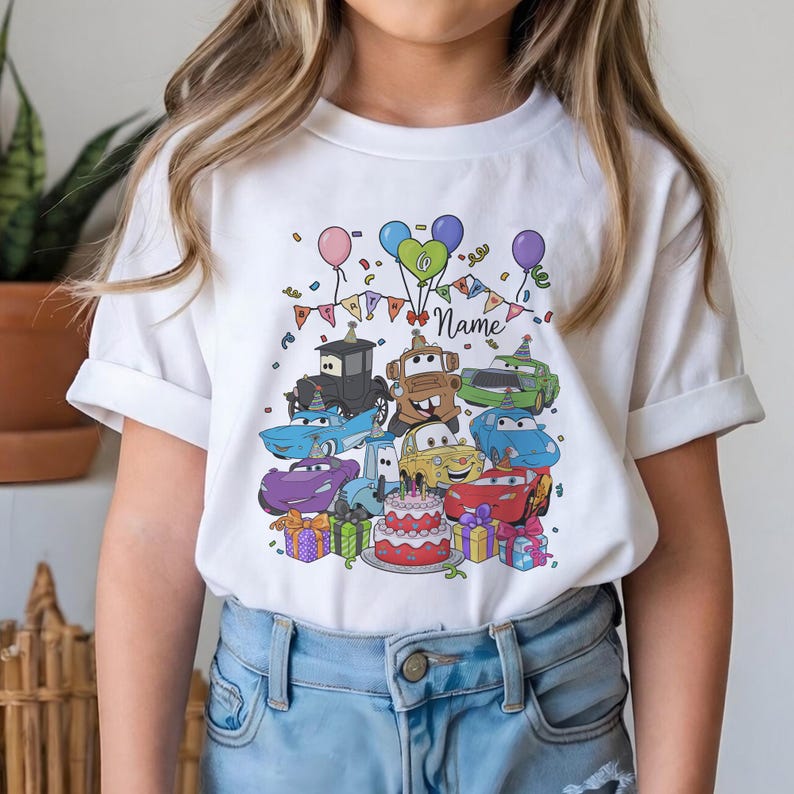 Peut inclure: T-shirt blanc avec un motif color&eacute; de voitures de dessins anim&eacute;s, de ballons, de confettis et d'un g&acirc;teau d'anniversaire. Le motif comprend le chiffre "6" et le mot "Name". Le t-shirt est port&eacute; par une personne.