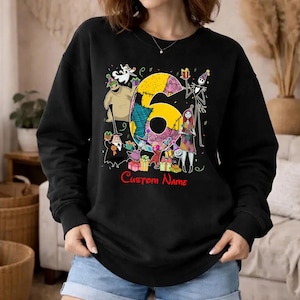 May include: A black long-sleeve sweatshirt featuring a large yellow number six surrounded by various animated characters in party hats and colorful gift boxes. The text Custom Name is printed in red below the graphic design.
