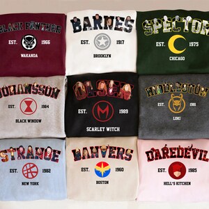 May include: Nine sweatshirts in various colours, including maroon, white, green, grey, black, light blue, and pink. Each sweatshirt displays a name, year, and location. The designs feature characters and logos. Measurements are not included.