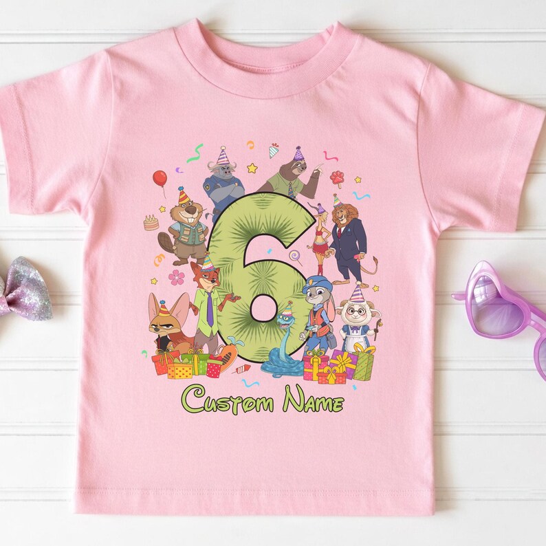 May include: A light pink short-sleeve t-shirt featuring a large green number six surrounded by various cartoon animal characters wearing party hats. The graphic includes colorful gift boxes, confetti, and the text Custom Name in green.