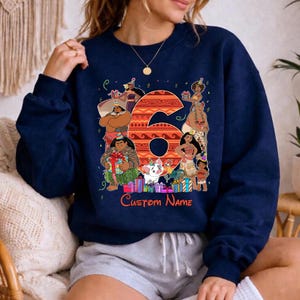 May include: A navy blue crewneck sweatshirt featuring a large orange patterned number six surrounded by various animated characters wearing party hats. The design includes colorful gift boxes and the red text Custom Name at the bottom.