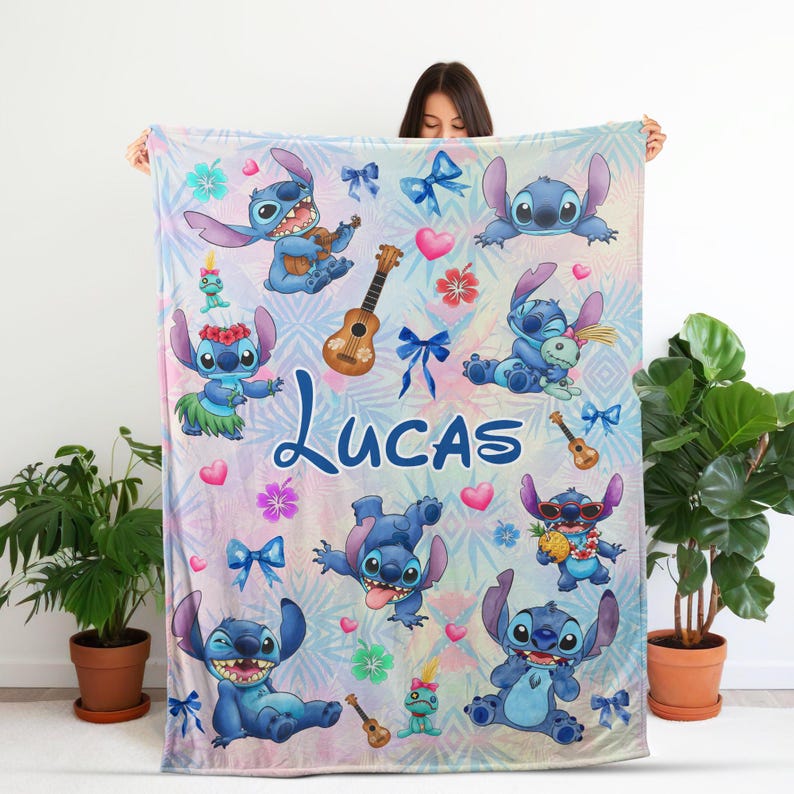 Op de afbeelding: Een gepersonaliseerde deken met het personage Stitch uit Lilo & Stitch. De deken heeft een pastelkleurige achtergrond met Stitch-illustraties, ukeleles, strikken en de naam "Lucas" in blauw schrift. Het ontwerp bevat harten en tropische bloemen.