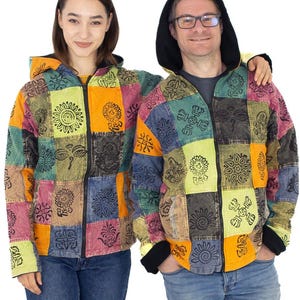 Może przedstawiać: Dwie osoby w kolorowych kurtkach w stylu patchwork z czarnym zamkiem błyskawicznym i kapturem. Kurtki mają różne wzory i projekty, w tym kwiaty, słońca i kształty geometryczne.