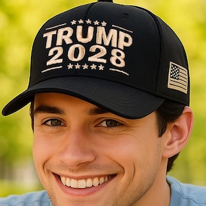 Könnte beinhalten: Schwarze Baseballkappe mit dem weißen Text "TRUMP 2028" und einem kleinen amerikanischen Flaggenaufnäher. Die Kappe wird von einer Person getragen, die ein hellblaues T-Shirt trägt. Ein weißer Kaffeebecher und ein Buch liegen auf dem Tisch.
