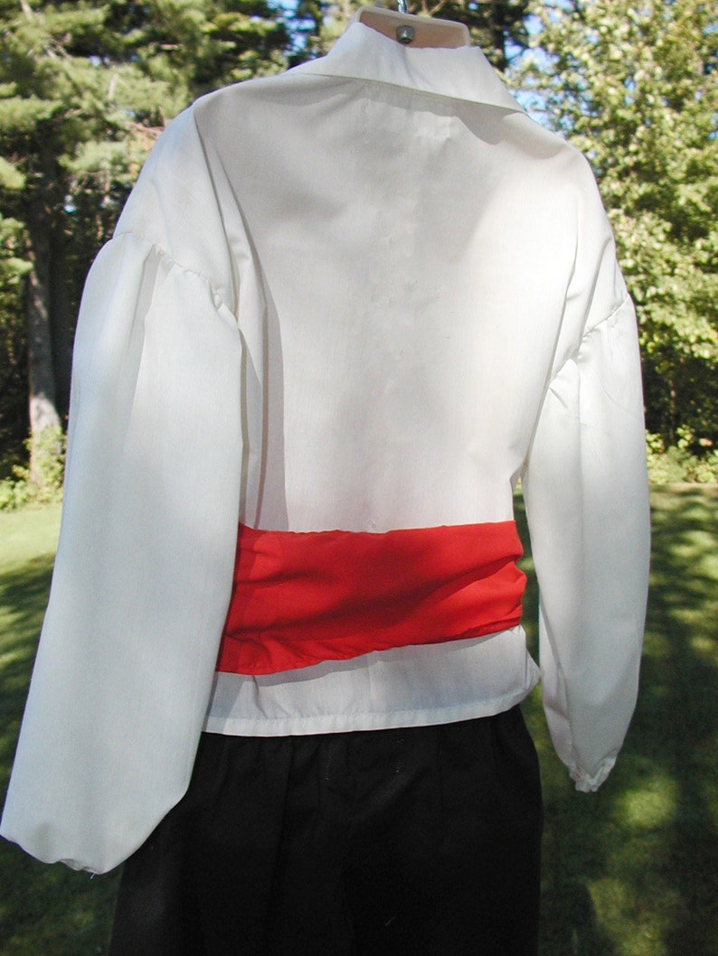 May include: White long-sleeved shirt with a red sash around the waist. The shirt has a gathered puff sleeve detail.