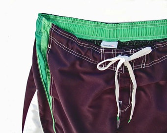 May include: Dark brown swim trunks with white stitching and a green elastic waistband. The waistband has the word "Speedo" printed on it.