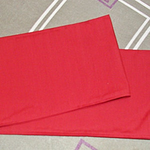 May include: A red fabric table runner, folded in half, with a smooth, even texture.