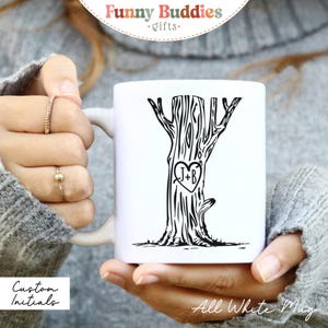 Peut inclure: Tasse en céramique blanche avec un motif d'arbre noir et une gravure en forme de cœur avec les initiales "J+B". La tasse porte le texte "Funny Buddies gifts" en haut et "Custom Initials" et "All White Mug" en bas.