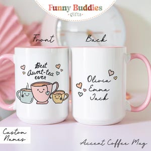 May include: White accent coffee mug with a pink handle and interior. The front of the mug says "Best Aunt-tea ever" with tea cup illustrations. The back of the mug has the names Olivia, Emma, and Jack. The mug has the text "Custom Names" and "Accent Coffee Mug".