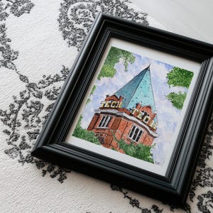 May include: A framed watercolor painting depicting a red brick building with a tall, pointed teal roof. The word TECH is displayed in yellow letters on two sides of the structure. Green trees surround the building against a light blue sky.